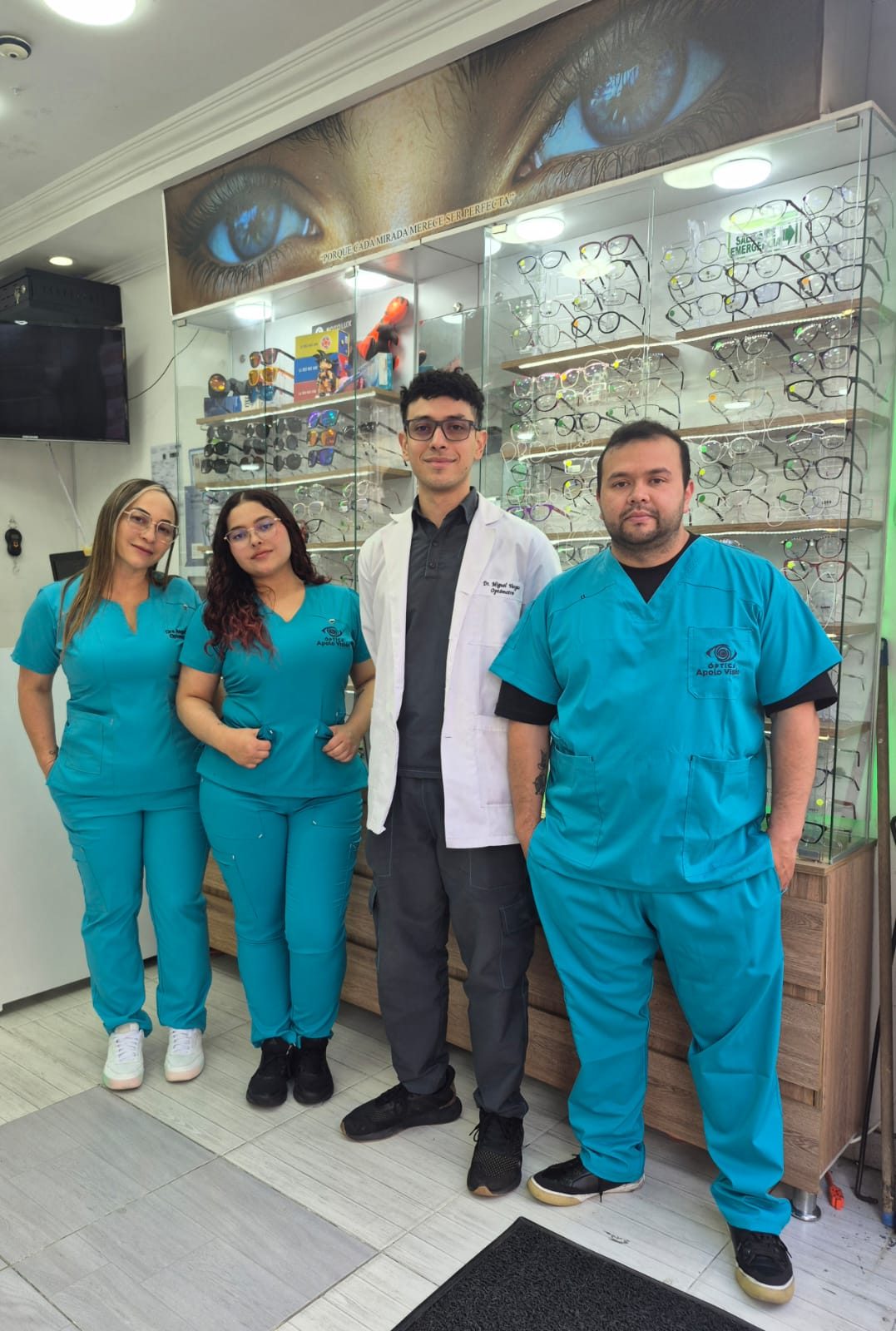 Equipo de Ópticas Apolo Visión en la sede de Bogotá: tres asesoras y asesores con uniforme y el optómetra con bata blanca, frente a las vitrinas de monturas